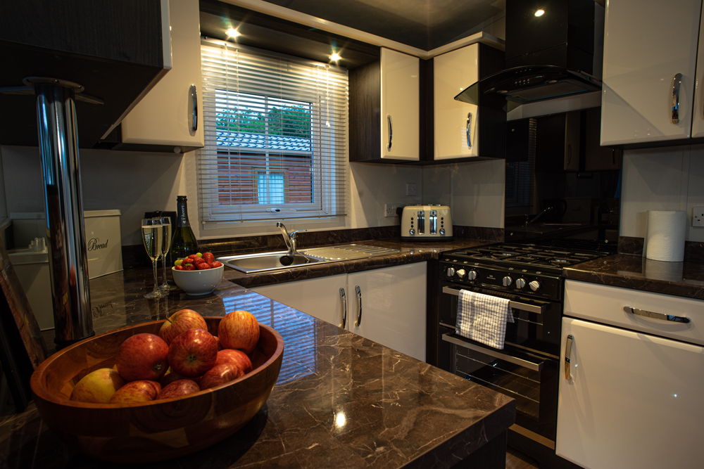 Modern kitchen with dark countertops, white and dark cabinets, fruit bowl, and stove.