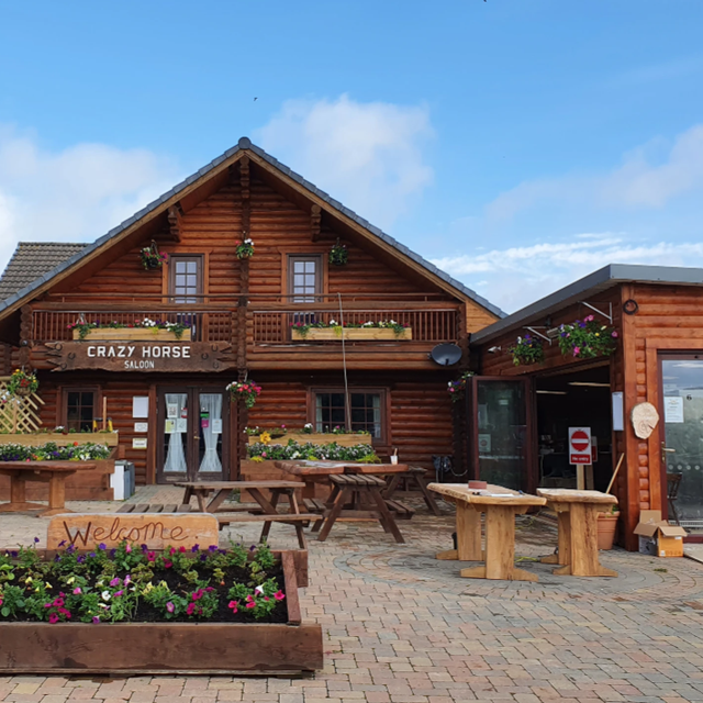 A log cabin restaurant called "Crazy Horse Saloon" with outdoor tables and flower boxes.