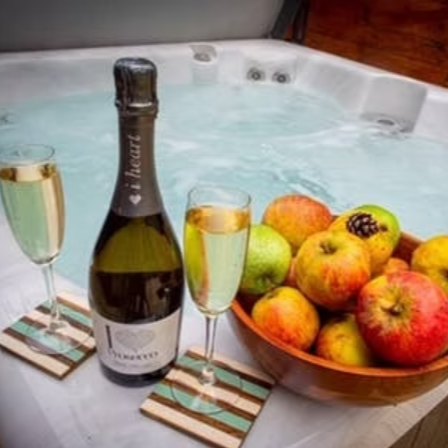 Champagne bottle, glasses, and fruit bowl next to a hot tub.