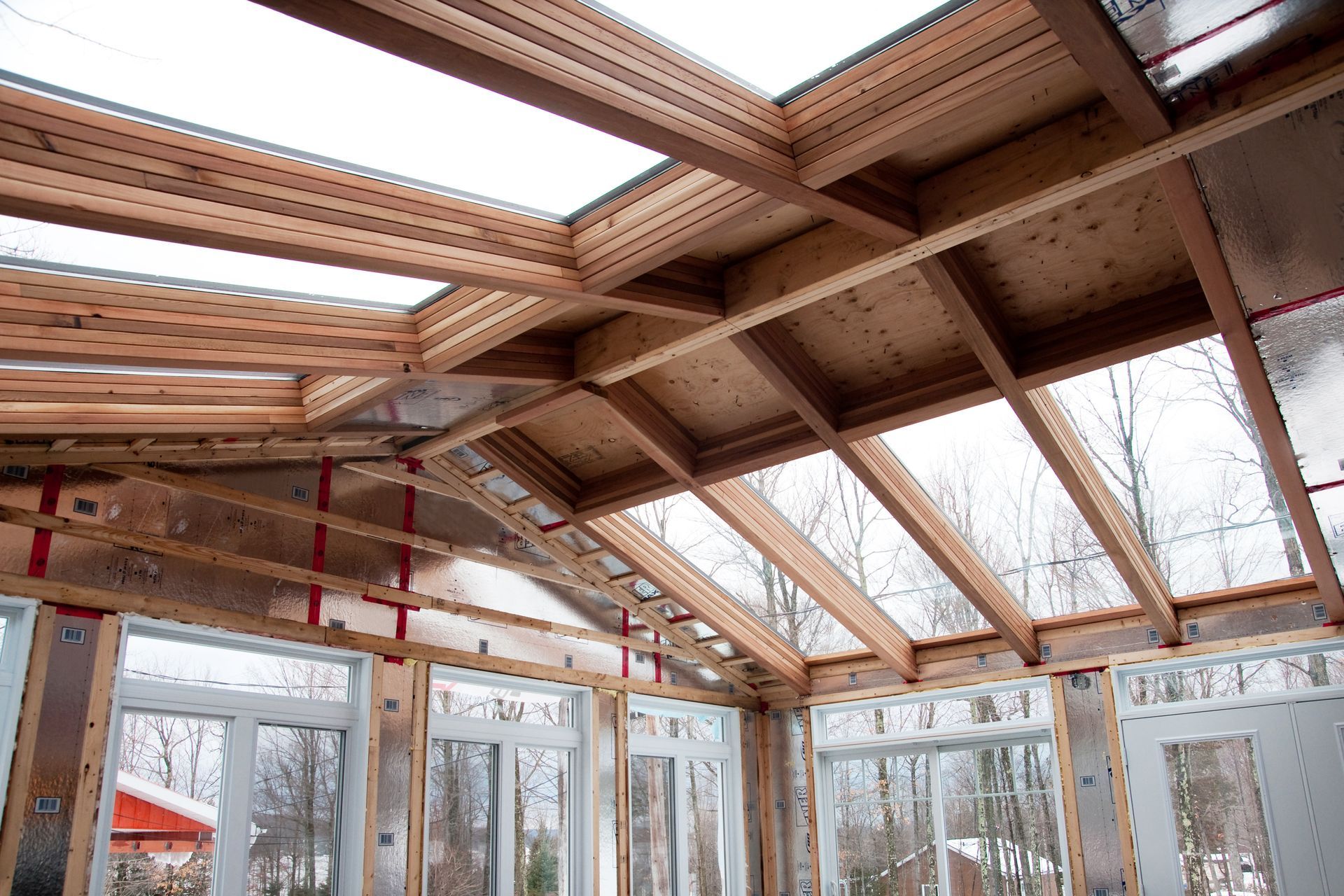 Intérieur d'une véranda en construction avec charpente apparente et puits de lumière.