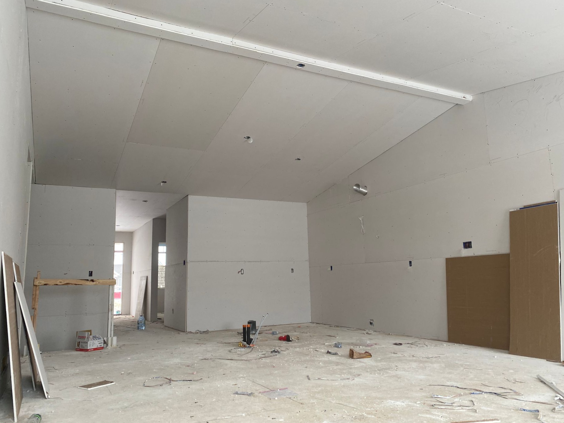 Pièce vide et inachevée avec cloisons sèches blanches, sol apparent et matériaux de construction.