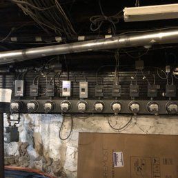 Electrical meters along a wall in a basement, with conduits and wiring overhead.