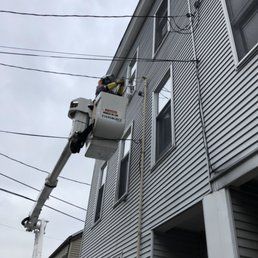 Worker in bucket truck servicing wires on a two-story building. Cloudy sky.