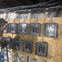 Person working on electrical boxes mounted on plywood wall. Wires are connected.