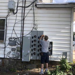 Electrician working on electrical panel attached to white building exterior.