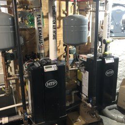 Two black HTP water heaters with pipes and tanks in a utility room.