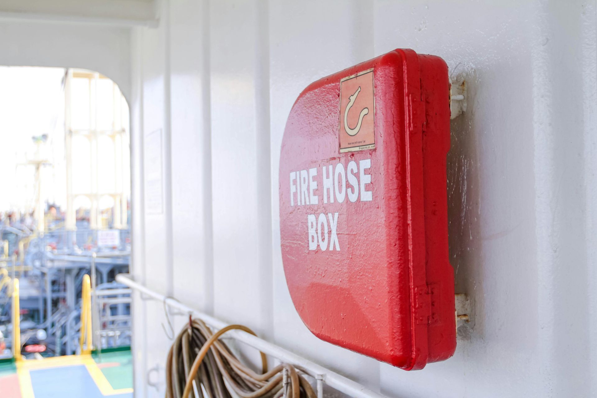 Red fire hose box mounted on a white wall on a ship deck.