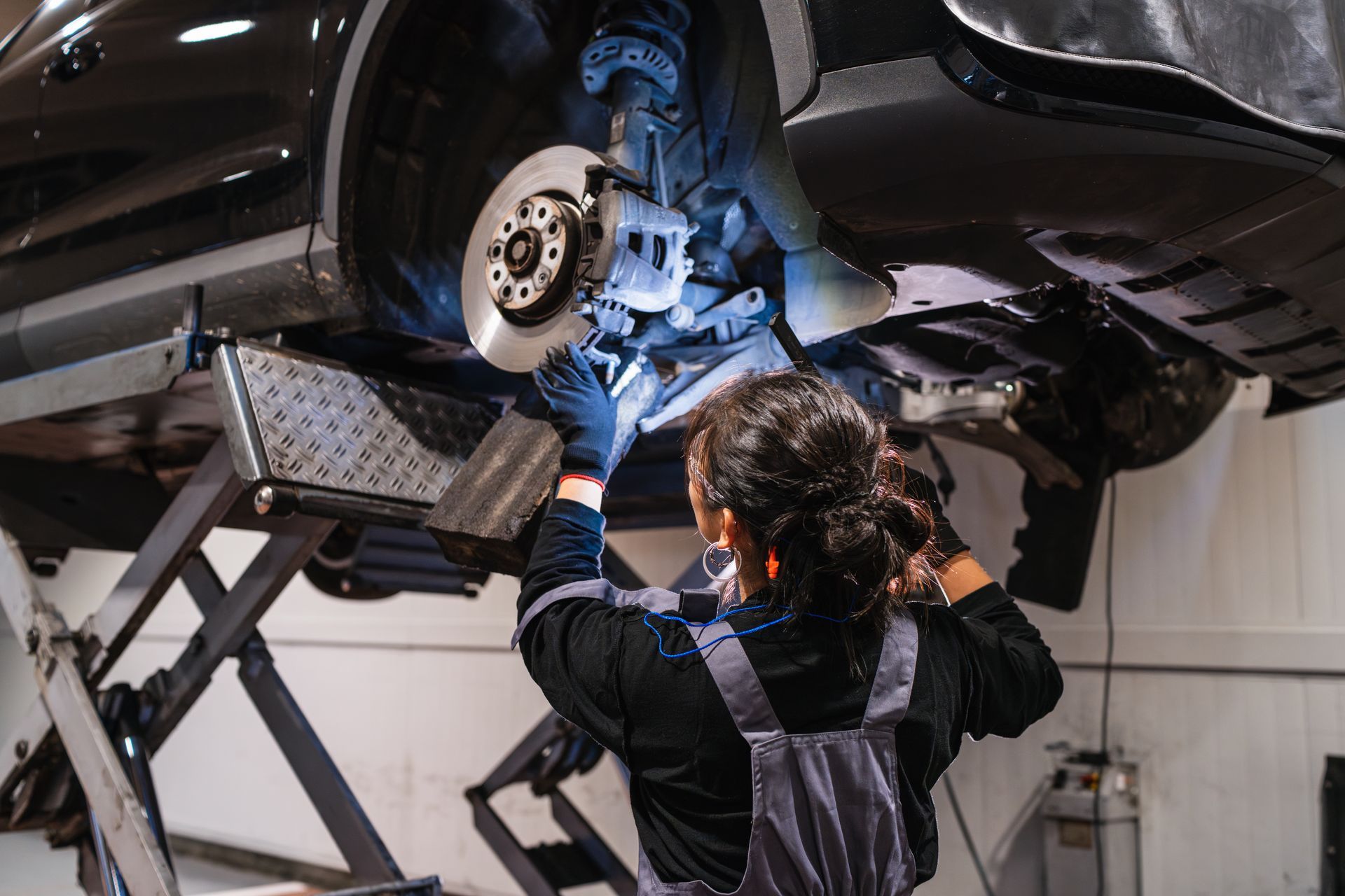 Mechanic working on a car's brakes, raised on a lift inside a garage.