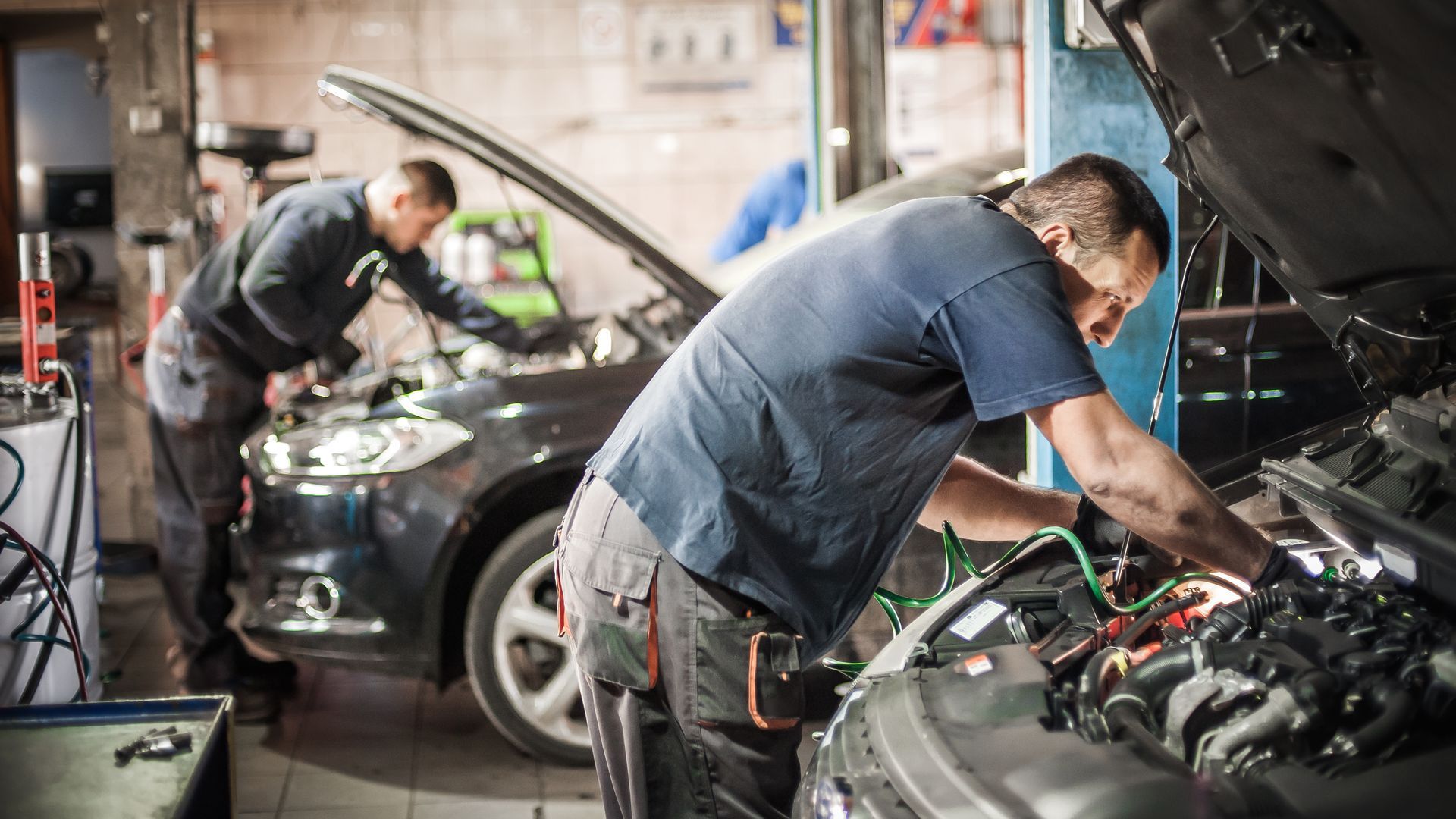 Mechanics working on cars in a garage, focusing on engines with hoods open.