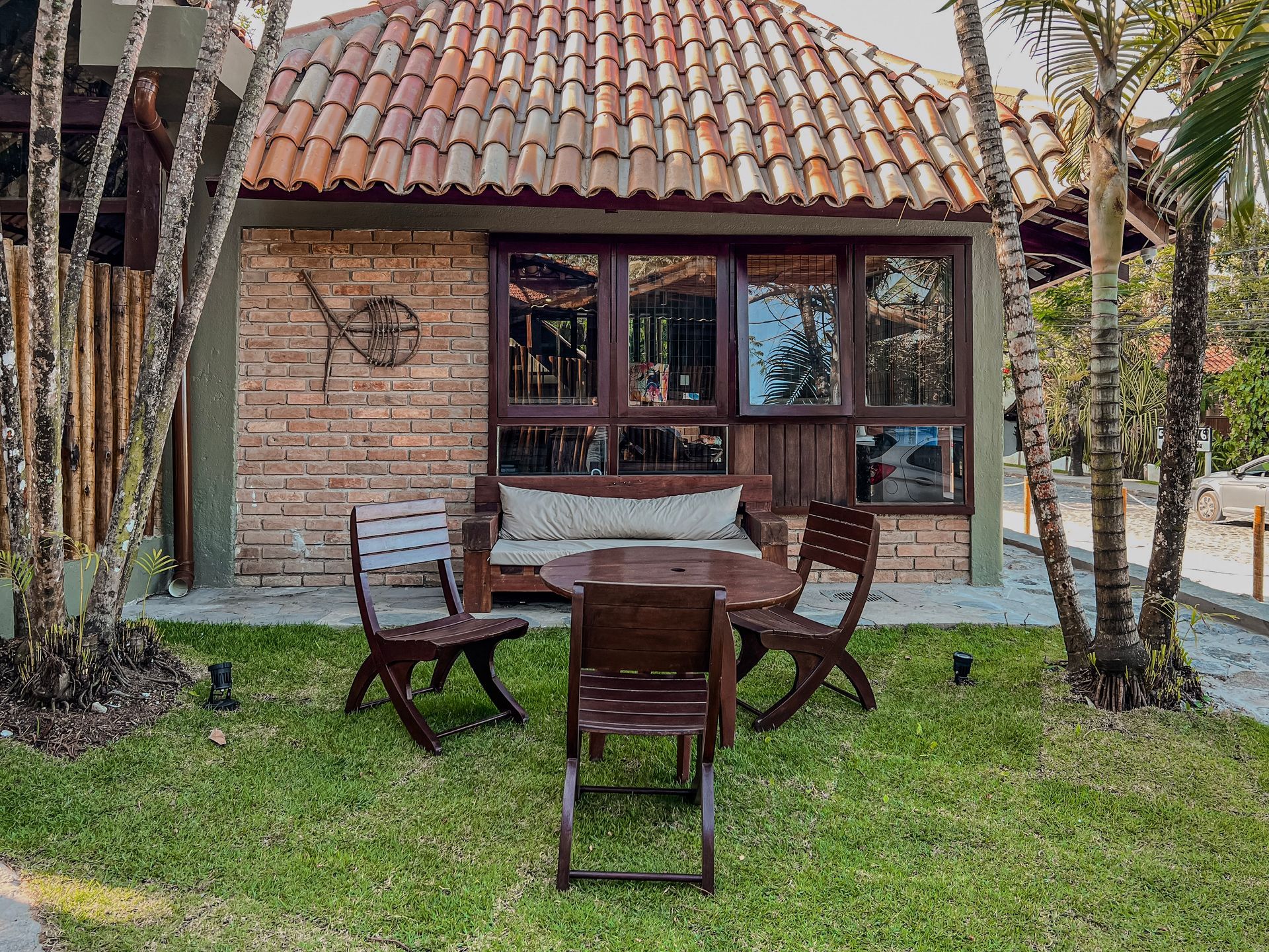Mobiliário de madeira para área externa sobre grama verde em frente a um prédio de tijolos com telhado de telha.