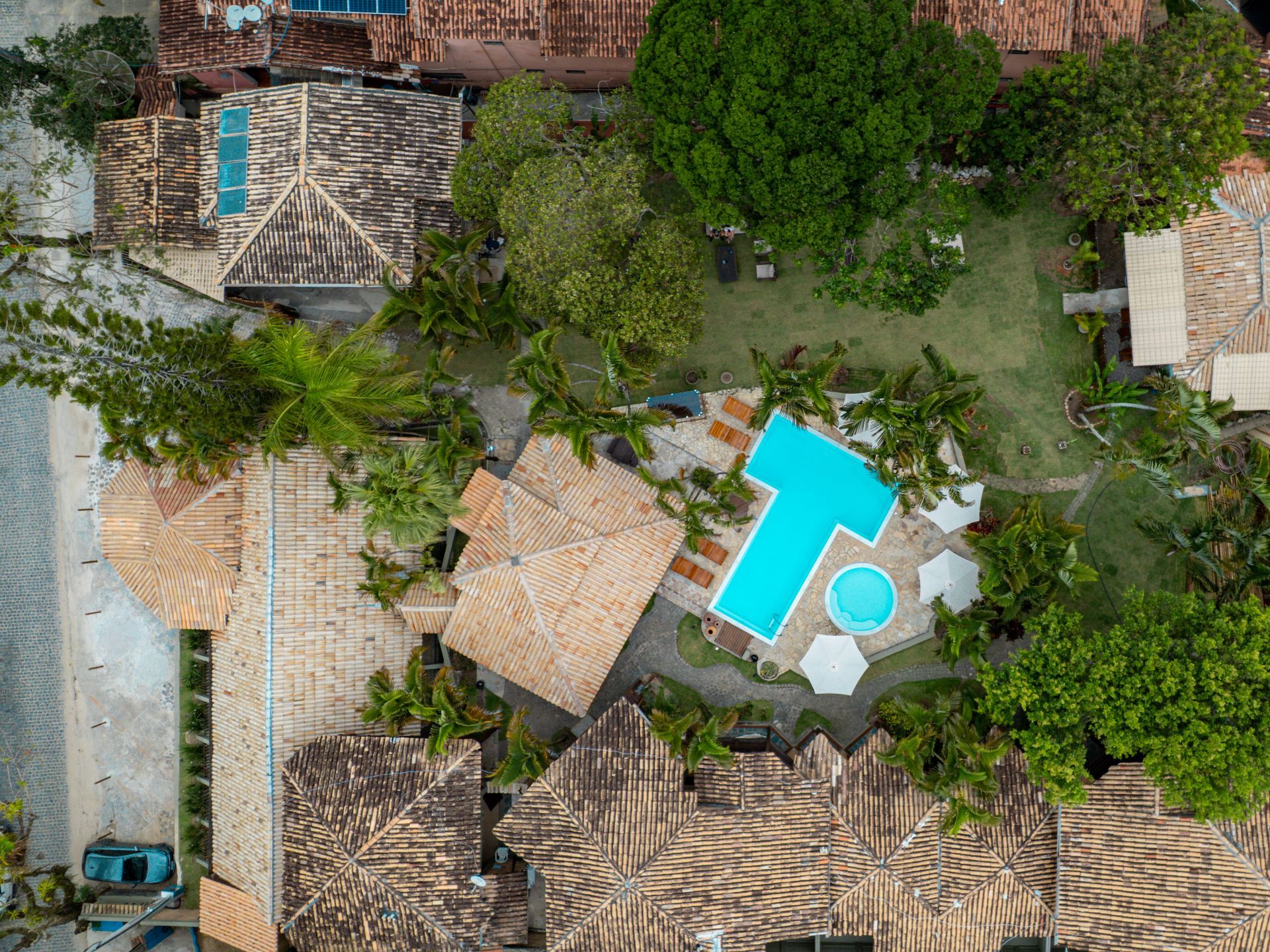 Vista aérea de um complexo com edifícios de telhados de telha, uma piscina azul, árvores e grama verde.
