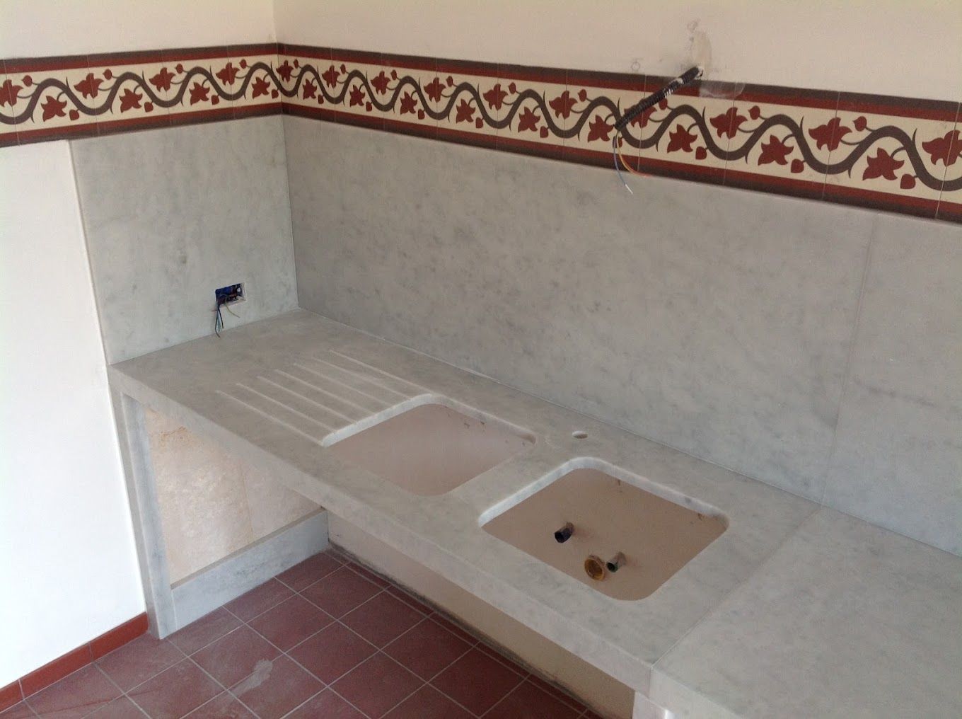 Una cucina con due lavelli e un bordo floreale sulla parete