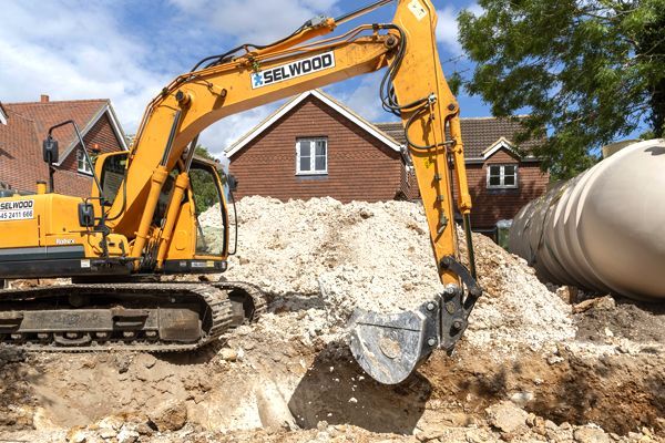 A yellow excavator is digging in a pile of dirt in front of a brick house.