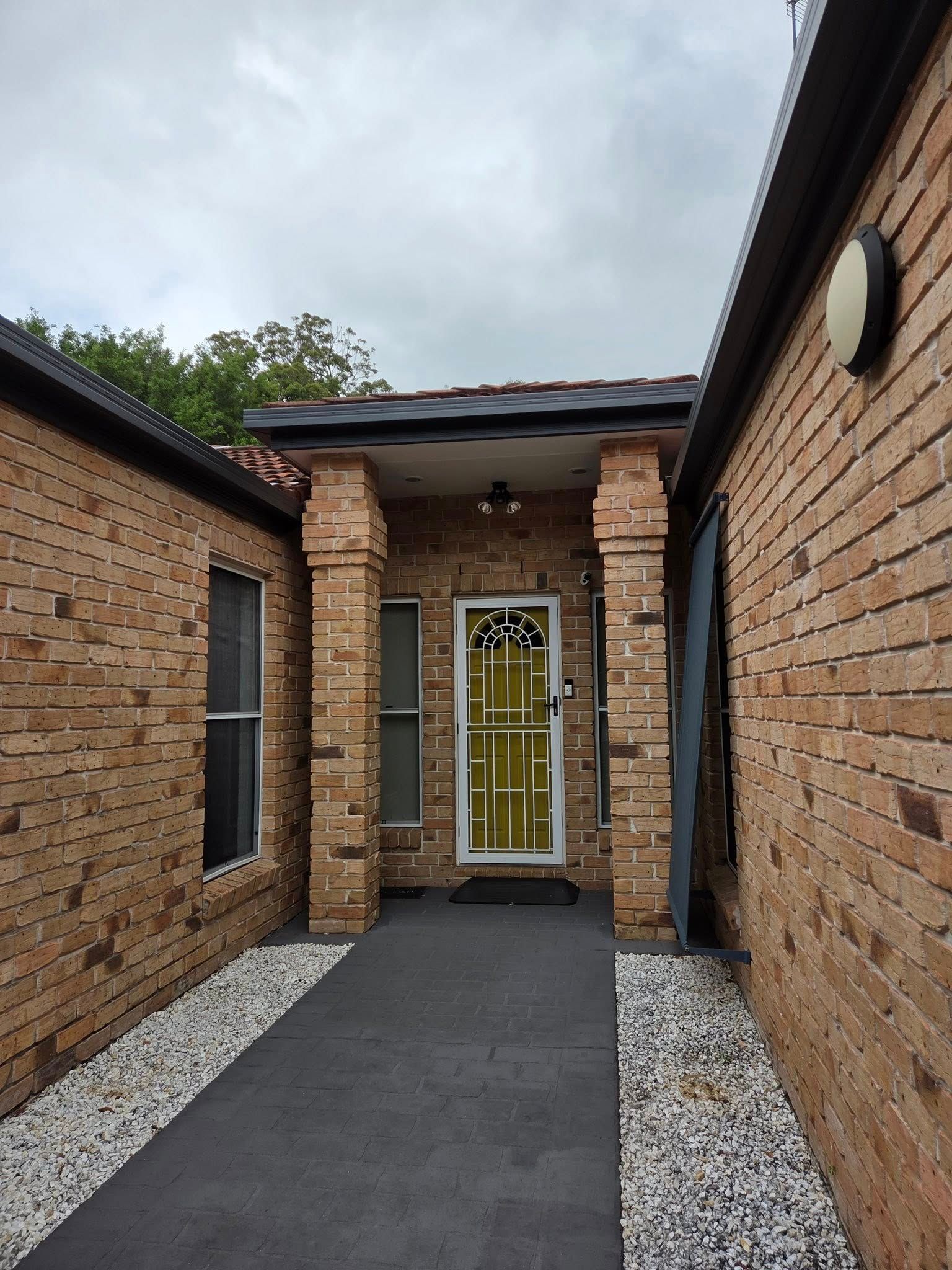 Brick Building Entrance With a Yellow Door, Covered Walkway, and Dark Path — MVP Painting Professionals in Coolum, QLD