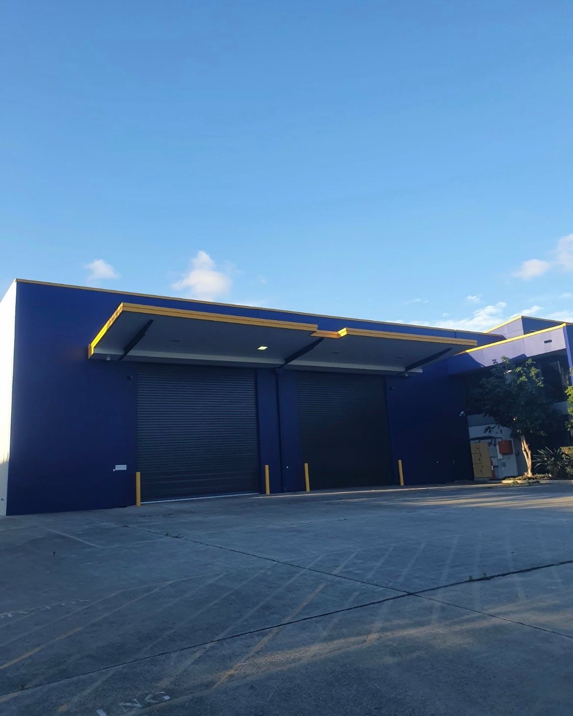 Blue Building With Two Roller Doors, Under a Yellow-trimmed Awning — MVP Painting Professionals in Noosa, QLD