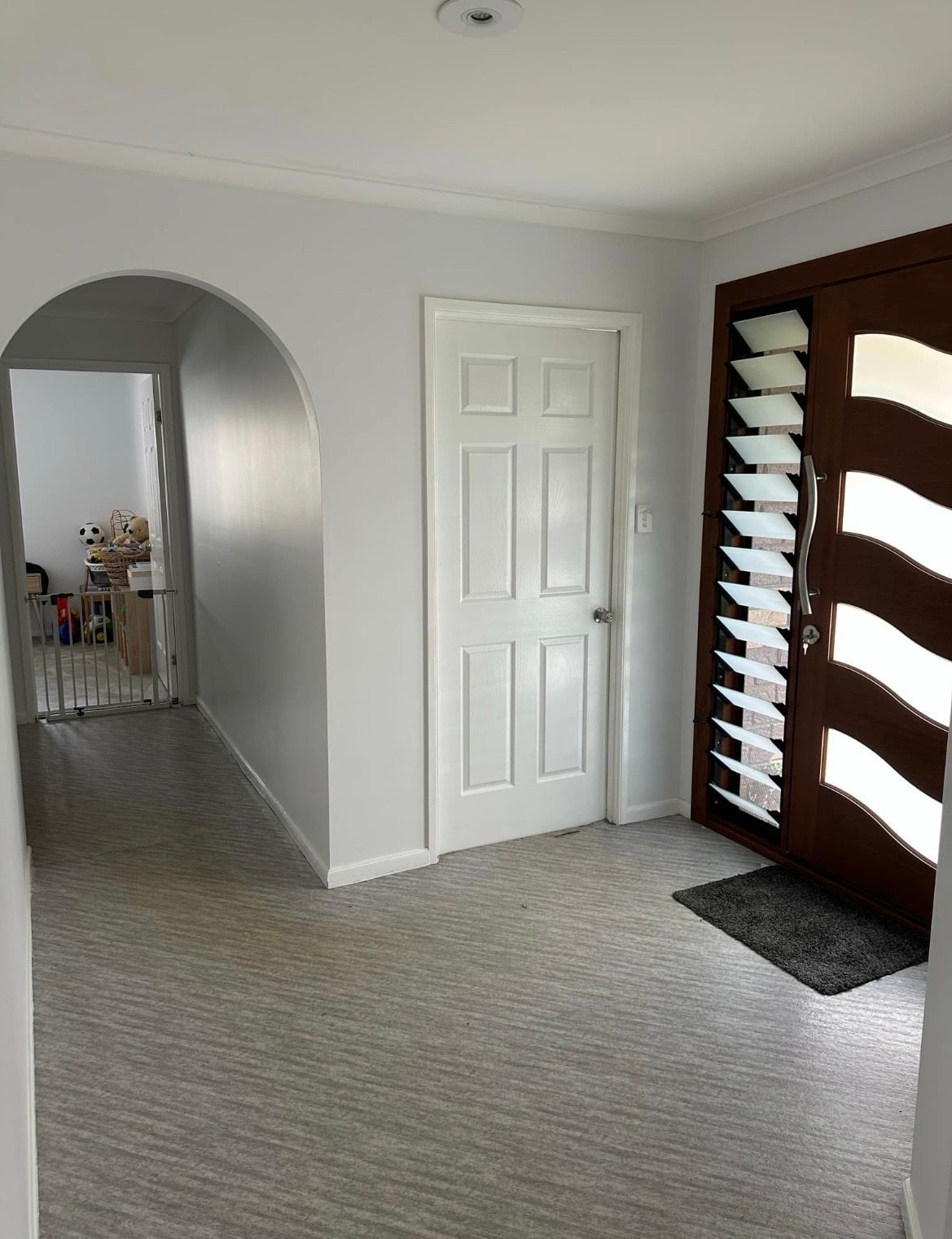 Entryway with gray floors, white door, and brown front door with blinds — MVP Painting Professionals in Kawana, QLD