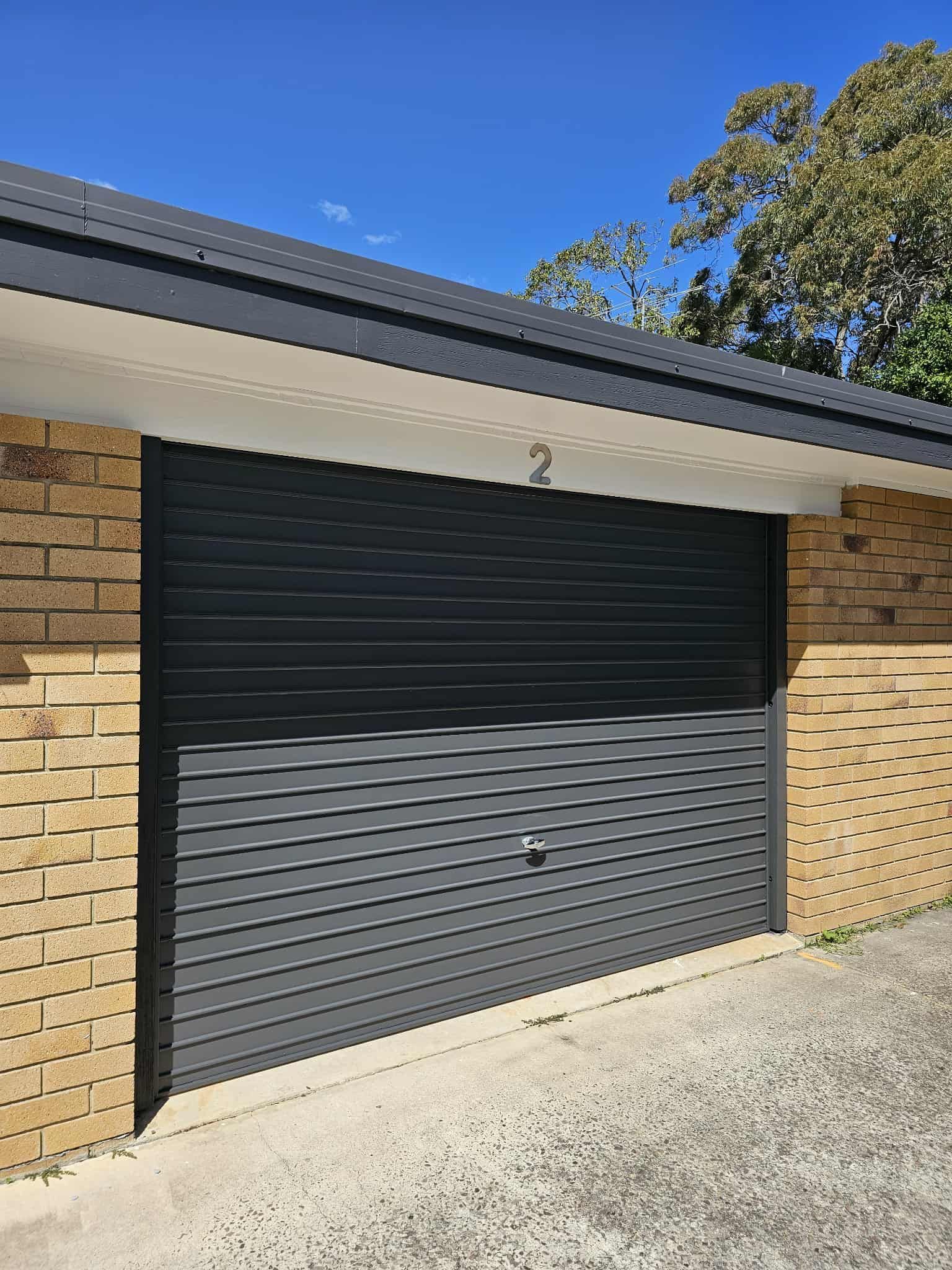 Dark gray garage door on a brick building with a blue sky background — MVP Painting Professionals in Maroochydore, QLD