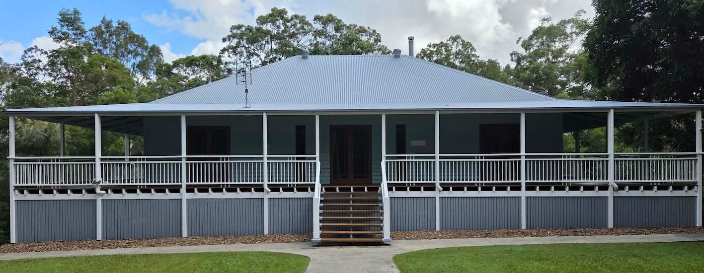 A gray house with a porch and steps, surrounded by green grass and trees, under a cloudy sky— MVP Painting Professionals in Sunshine Coast, QLD