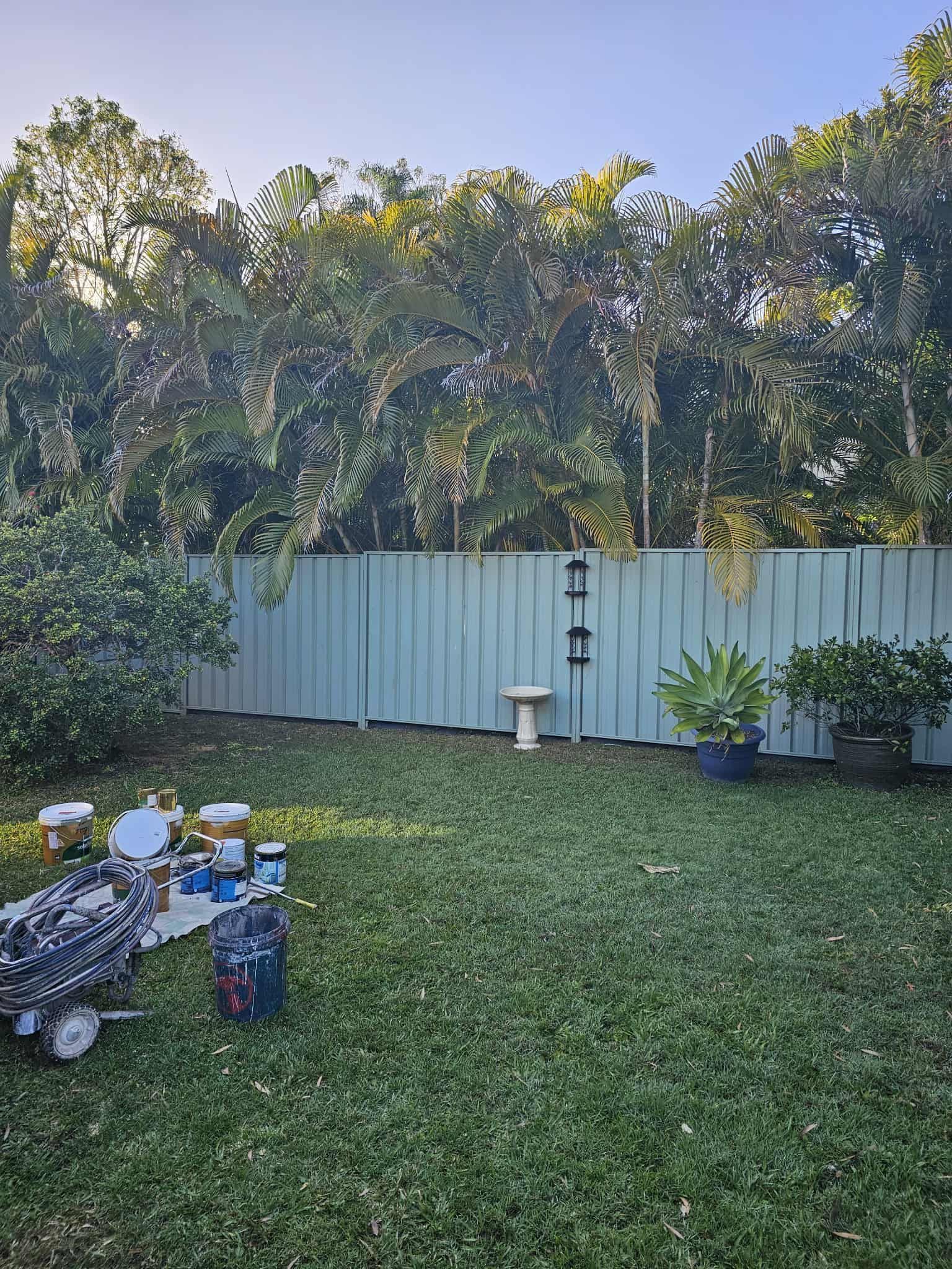 Backyard With a Light Blue Fence, Lawn, Trees, Paint Supplies, and a Birdbath — MVP Painting Professionals in Caloundra, QLD