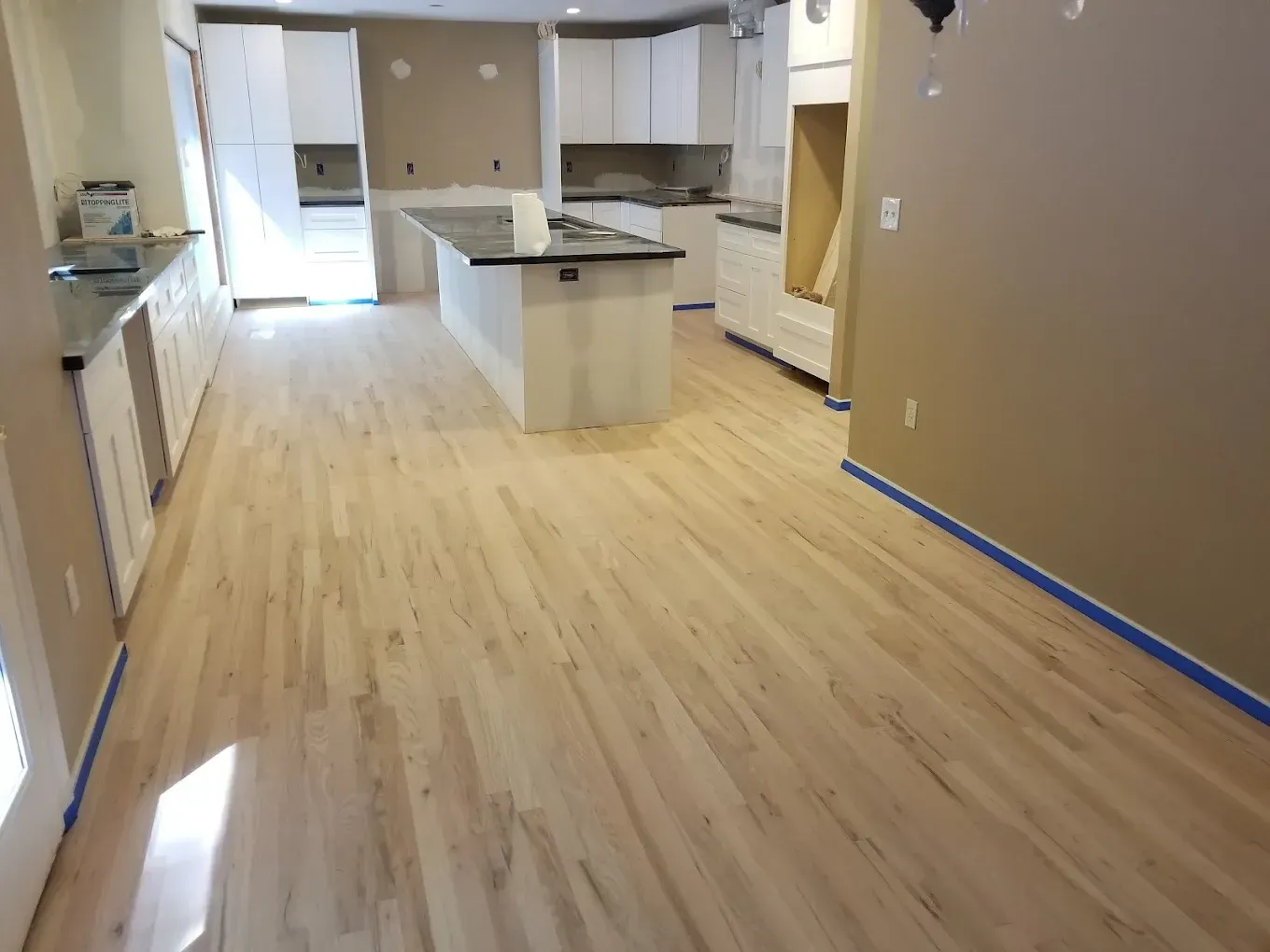 Newly installed light wood flooring in a kitchen with white cabinets, a central island, and granite countertops.