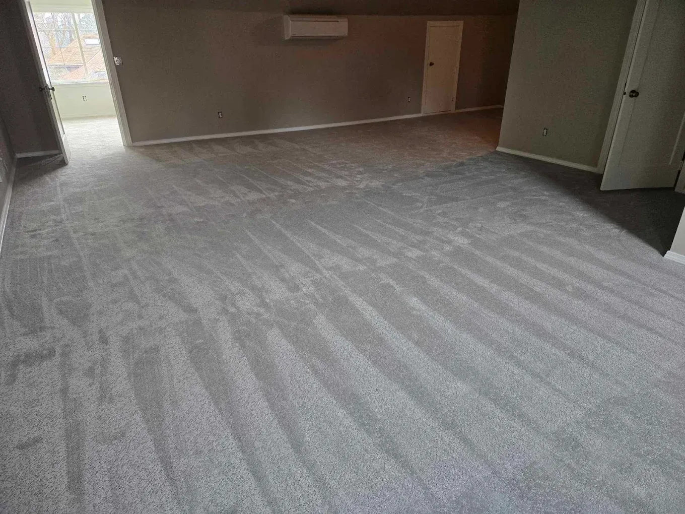 Gray carpeted room with light gray walls, an open doorway, and a closed white door.
