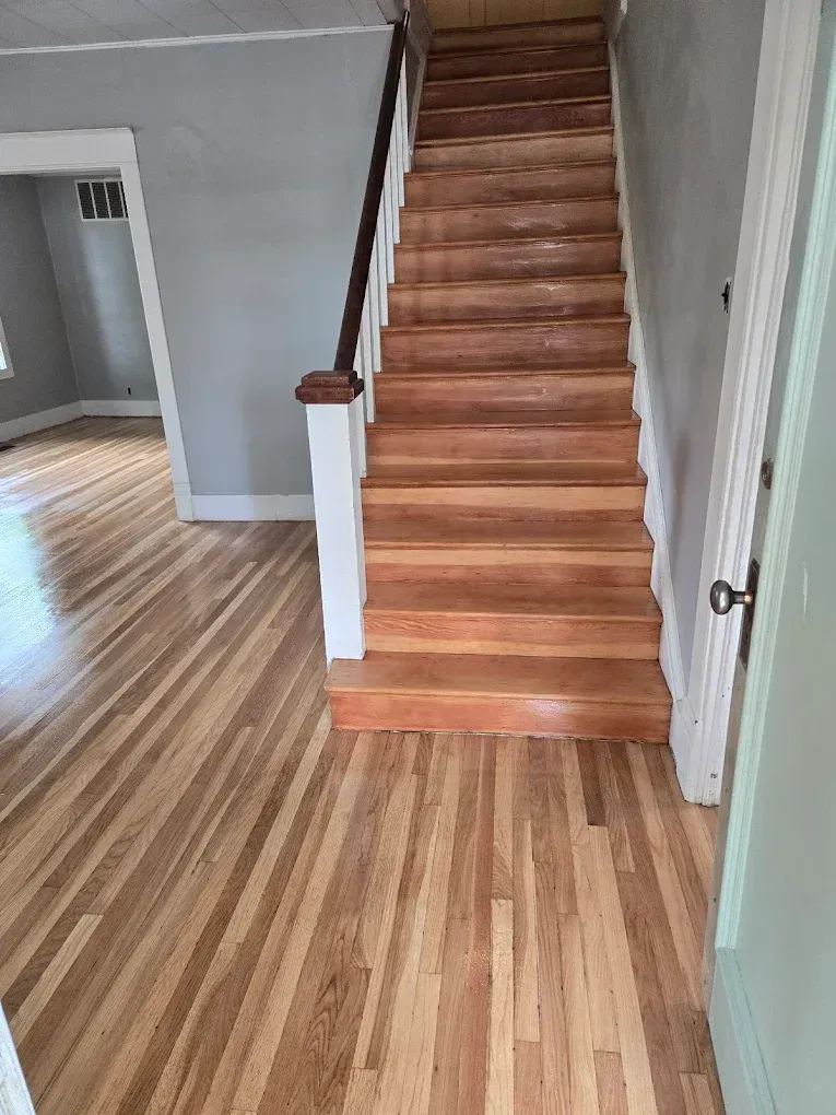 Wooden staircase with hardwood floors in a home. The stairs have a dark brown handrail.