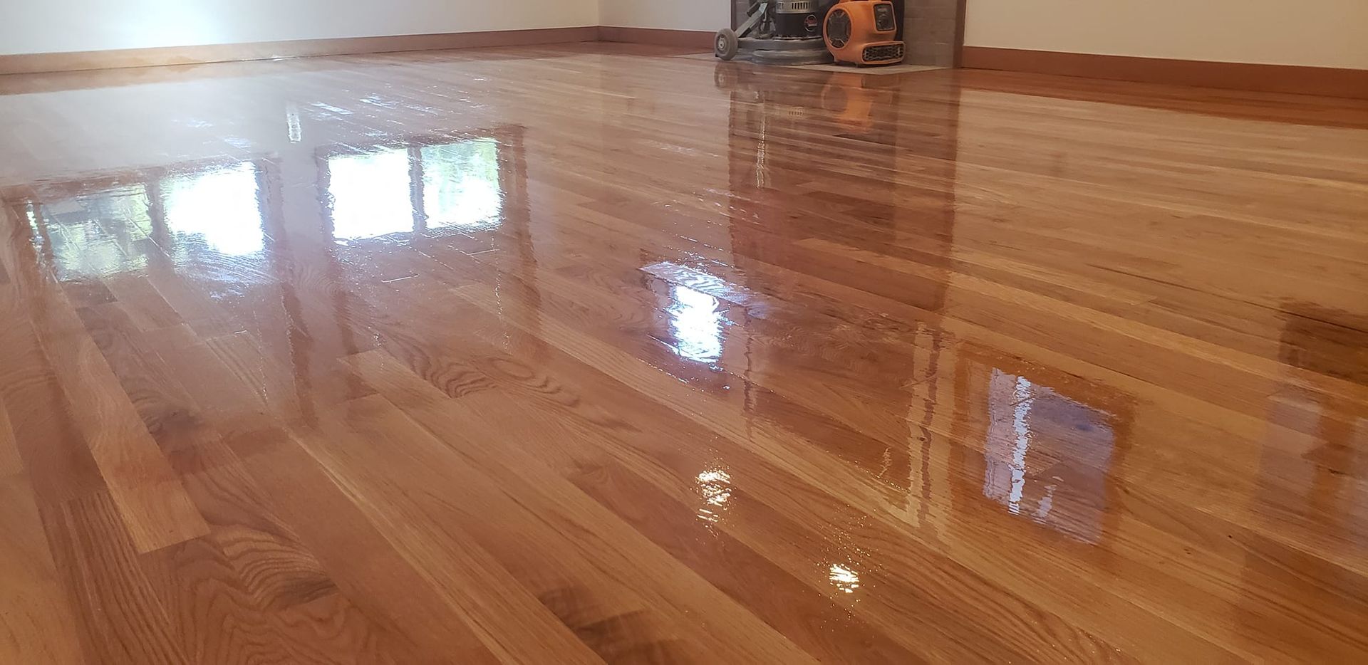 A recently polished wooden floor reflects light and a nearby window. A machine sits in the corner.