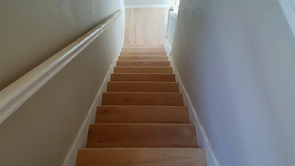 Wooden staircase with white handrail ascending between light gray walls.