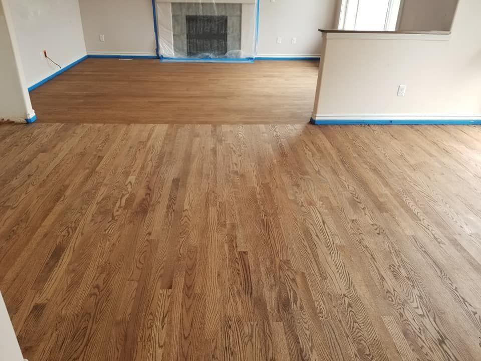 Newly installed hardwood floors in a home. The wood has a brown stain. Blue tape lines the wall baseboards.