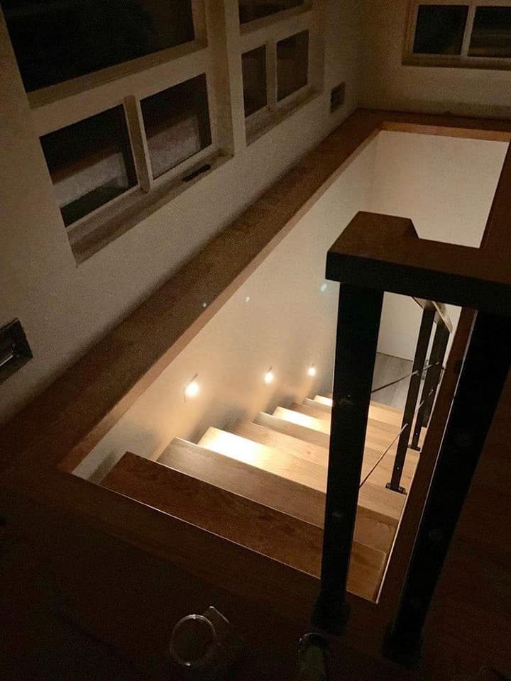Wooden staircase with built-in lights, descending into a lower level. Handrail on the right.