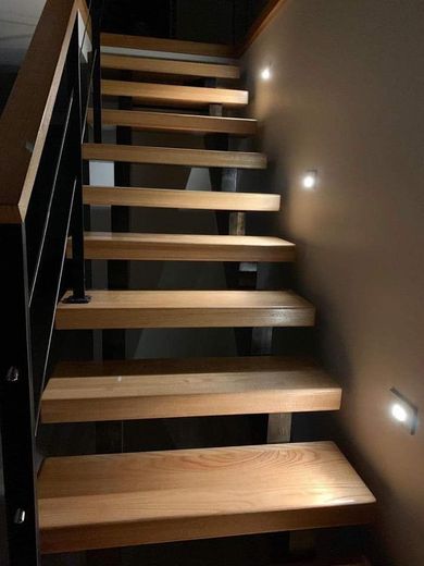 Wooden staircase with black metal railing and wall-mounted lights.