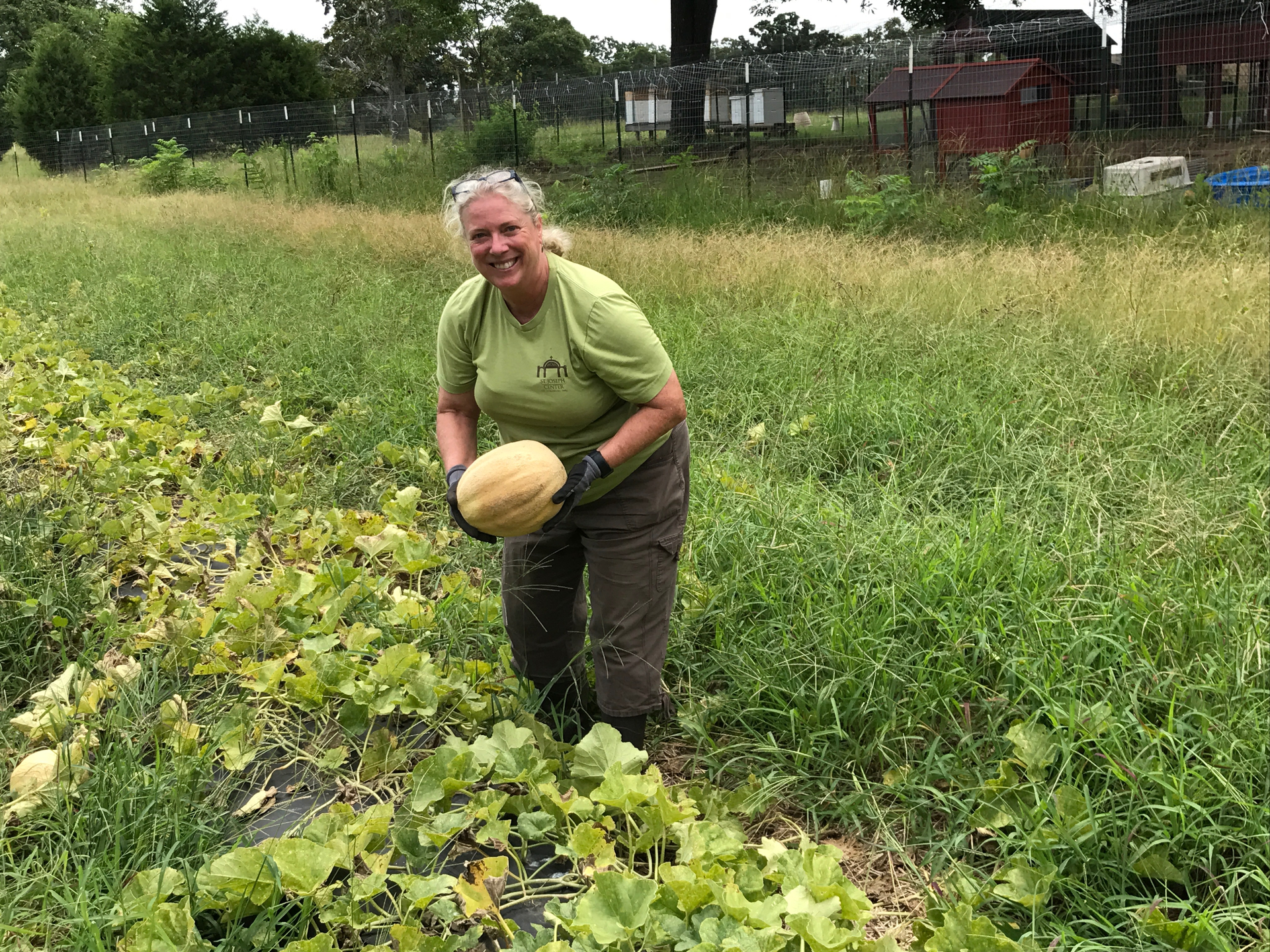 A woman is standing in a field holding a melon.