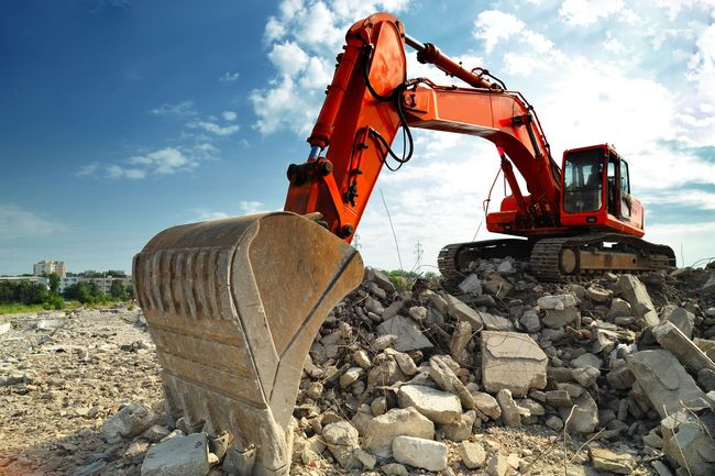 A red excavator is working on a pile of rocks.