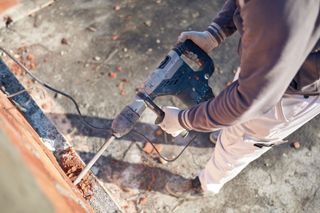 A man is using a hammer drill to drill a hole in a wall.