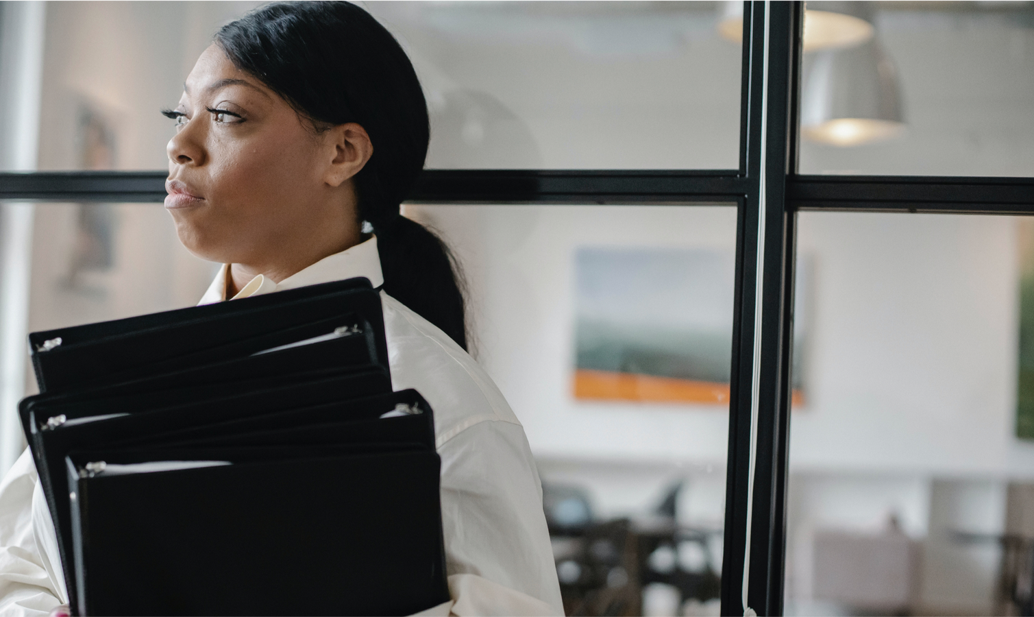 A woman is standing in front of a window holding a stack of folders.