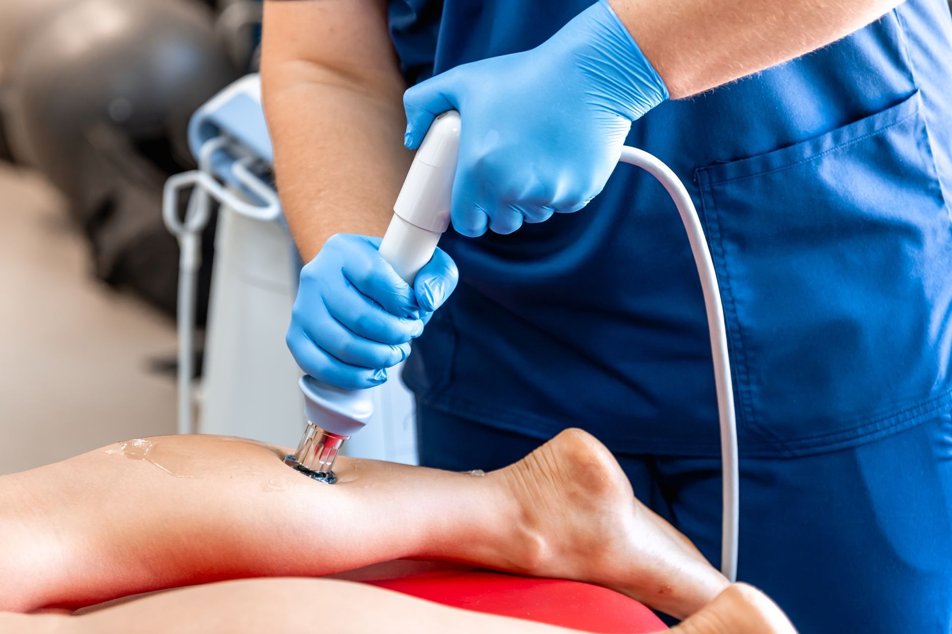 A person in blue gloves using a medical device on a person's leg.