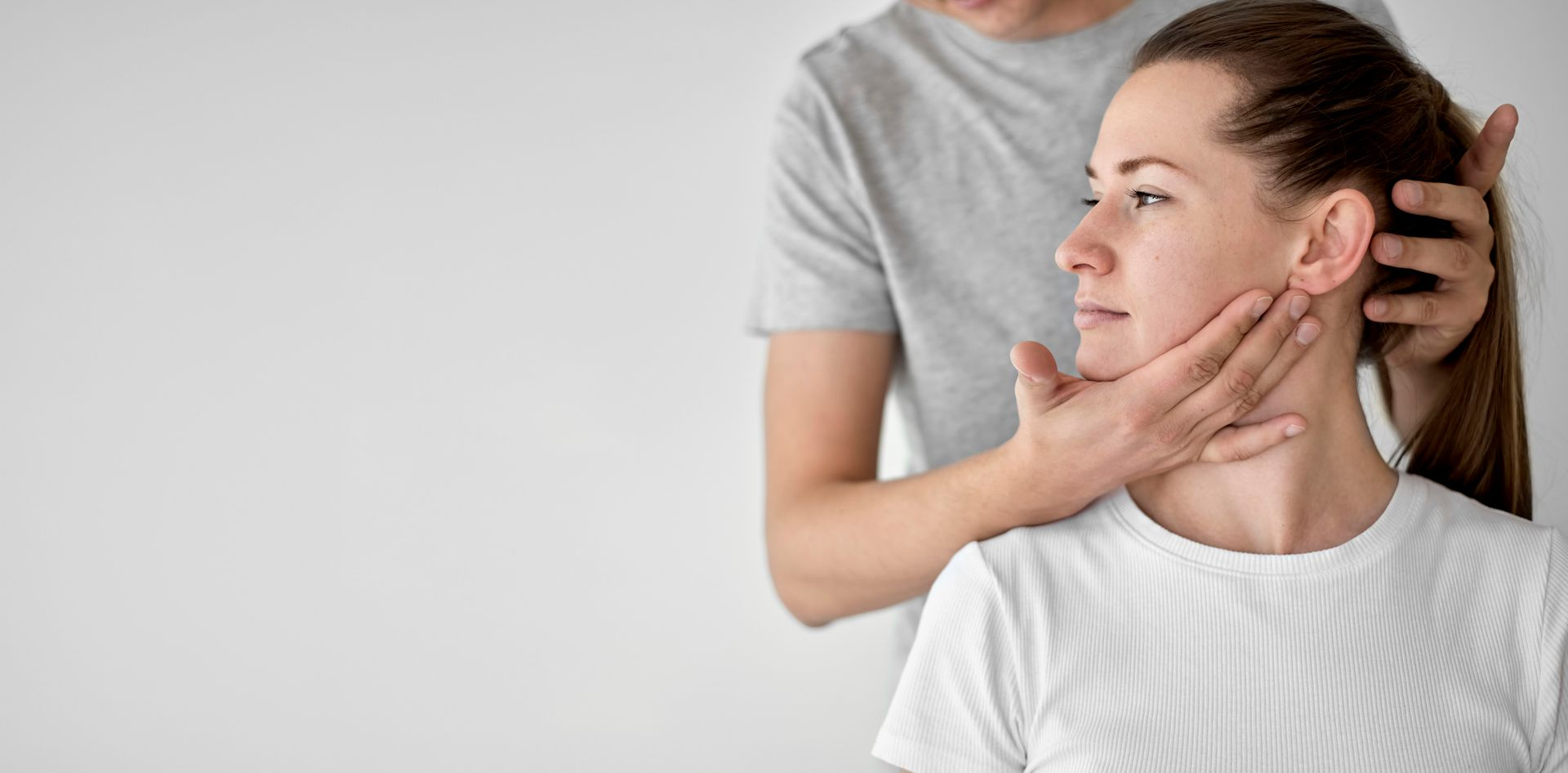A person is holding another person's head and jaw to evaluate their neck's movement.