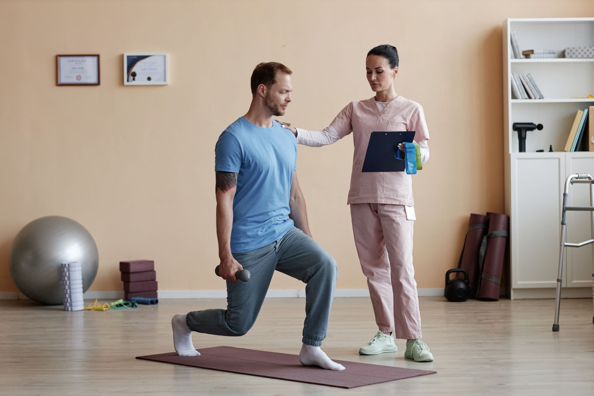 A physical therapist guides a patient performing a weighted lunge on a yoga mat in a clinical rehabilitation room.