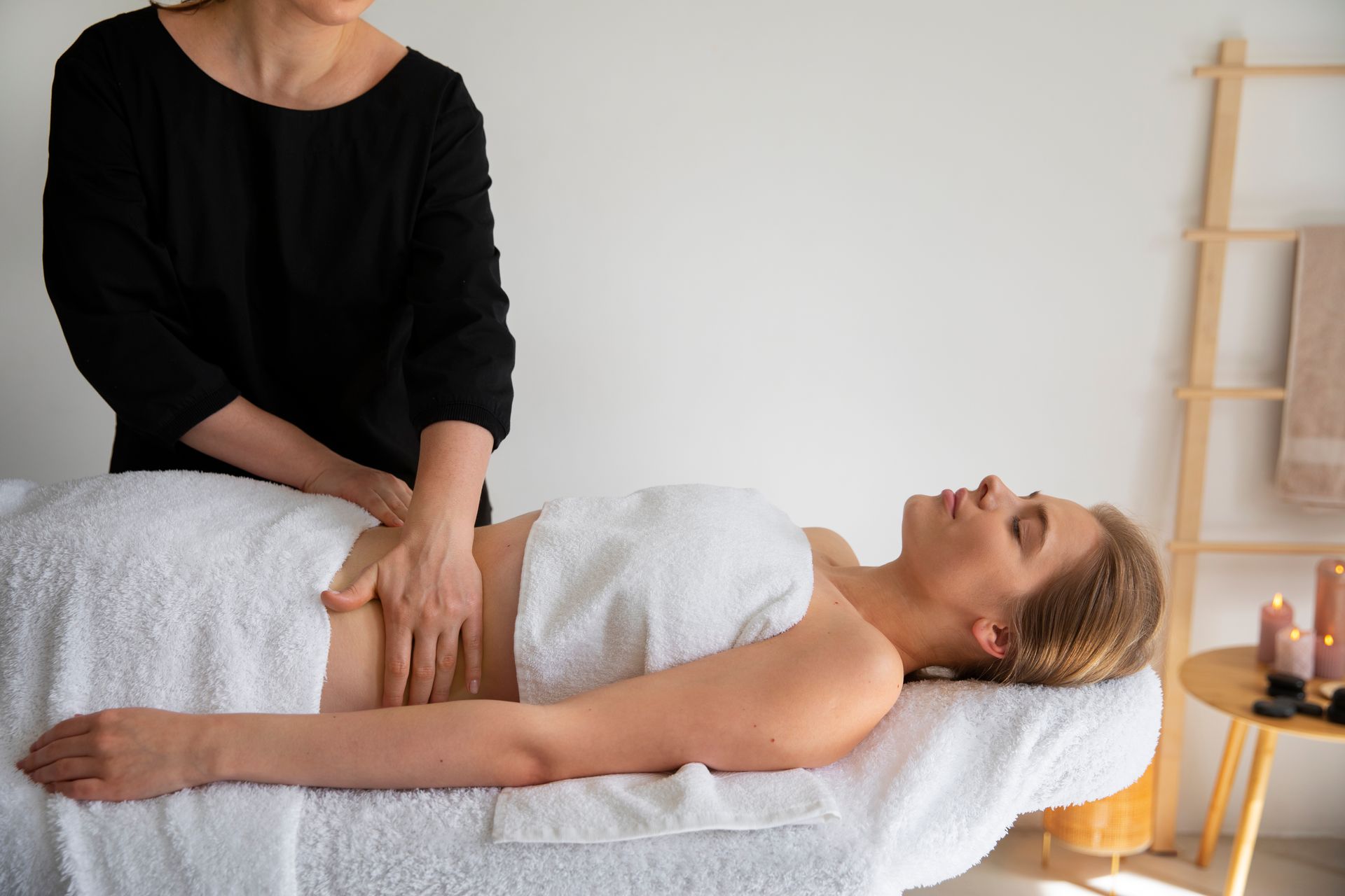 A person receives a professional abdominal massage while lying on a table in a spa setting.