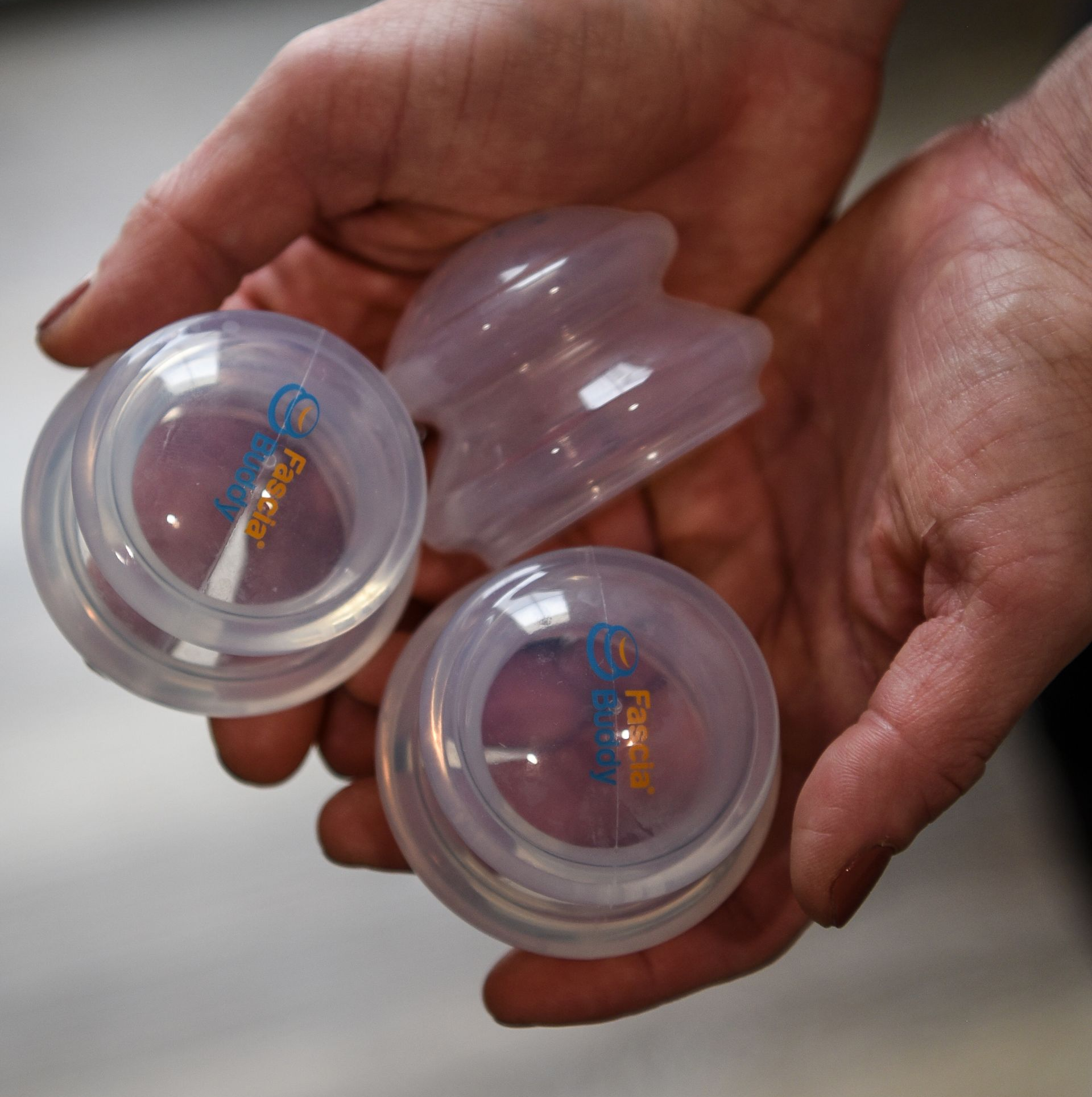 Hands holding cupping therapy tools: clear cups and scraping tools.