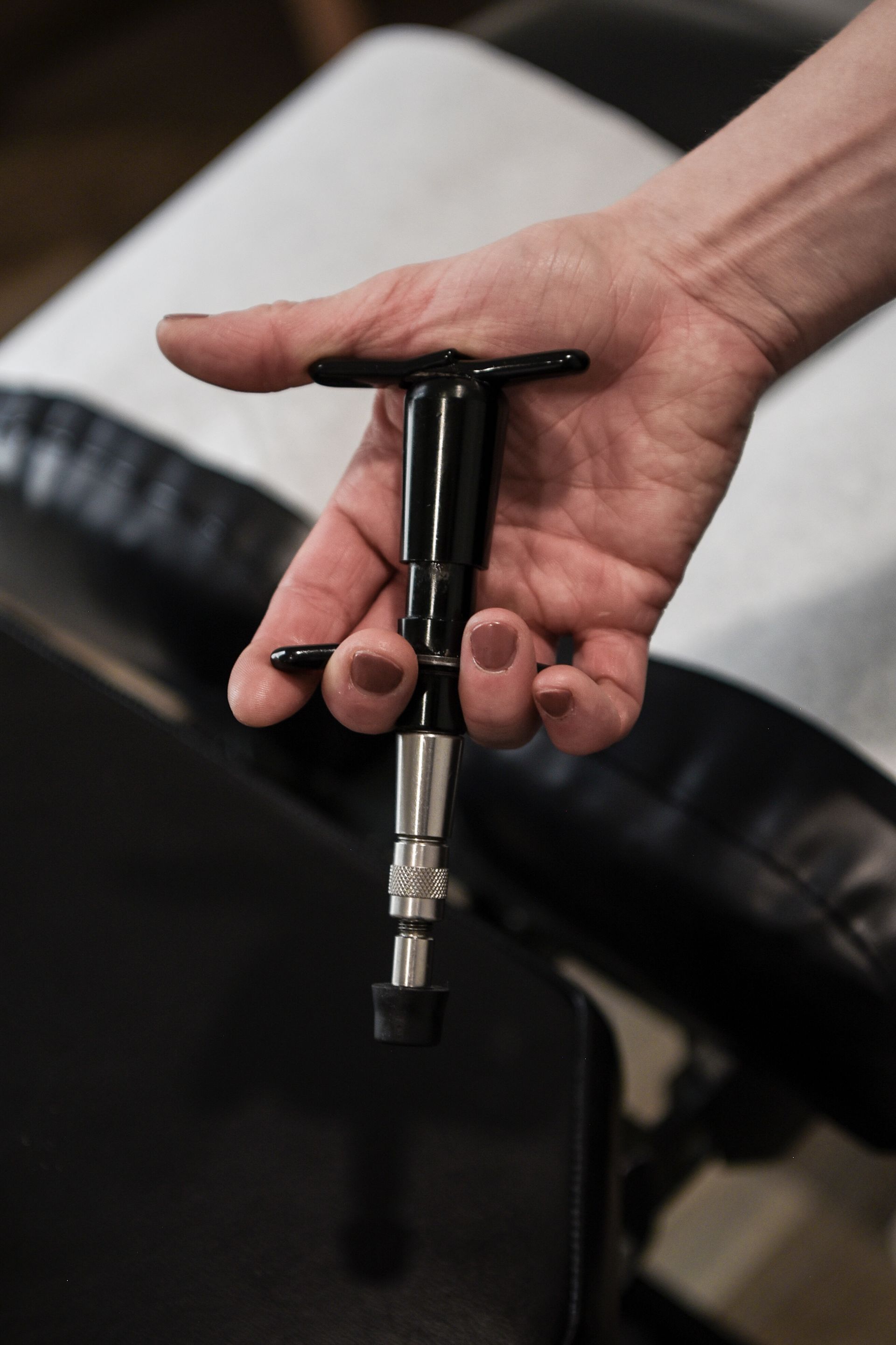 Hand holding a black chiropractic adjusting tool over a black padded surface.