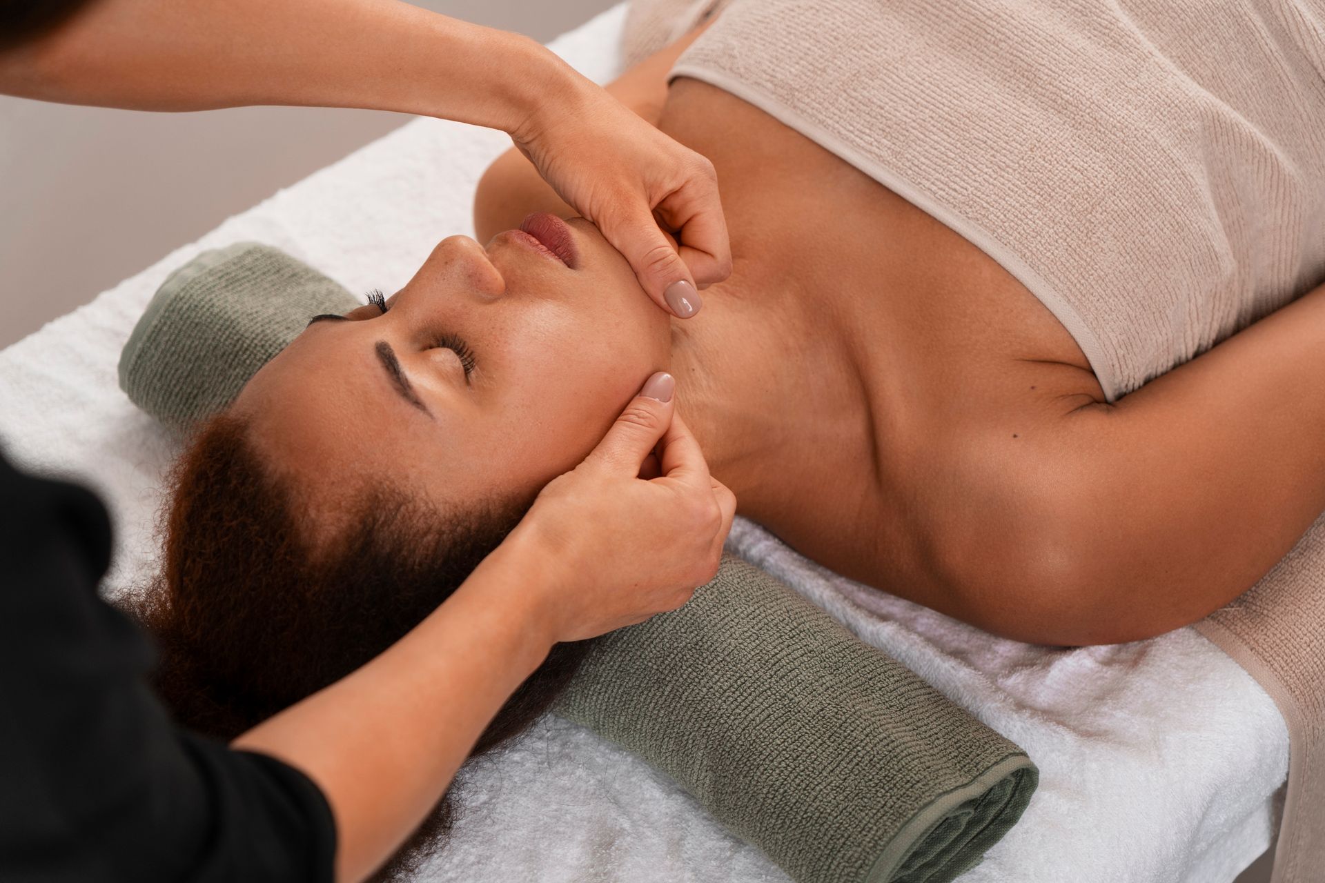 A spa therapist performs a facial massage on a client lying on a treatment table.