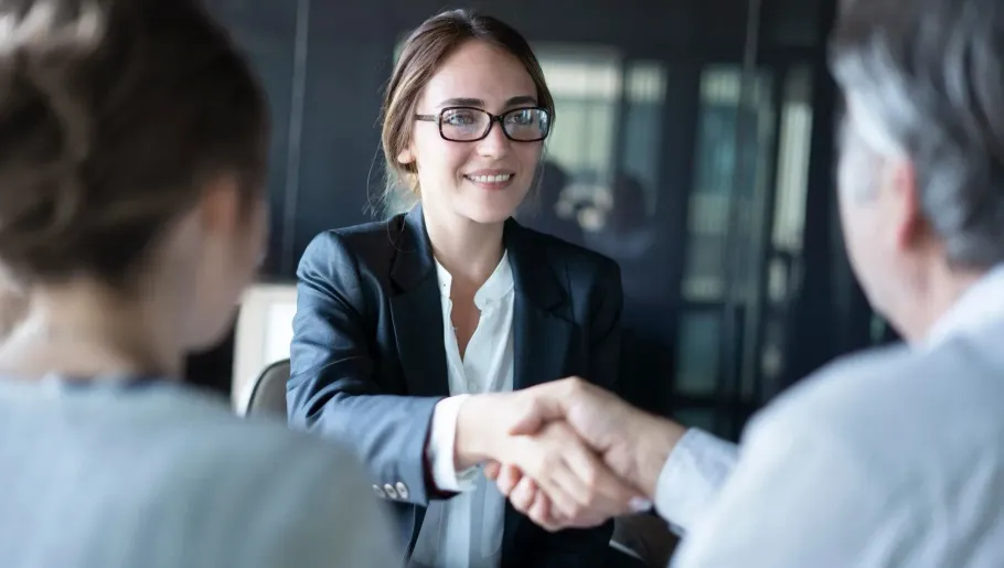 Female attorney smiling while shaking hands with a client in a modern office