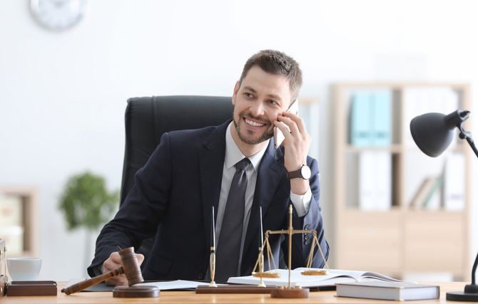 Male lawyer in a suit smiling while talking on the phone at his office desk.