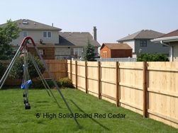 6' high solid red cedar fence surrounds a grassy backyard with a swing set. Houses are in the background.