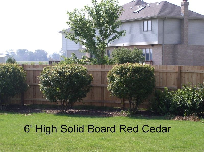 6' red cedar fence with shrubs in front of a house with a green lawn.