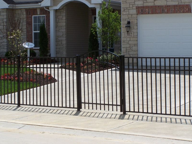 Black metal fence with gate in front of a house, blocking a driveway.