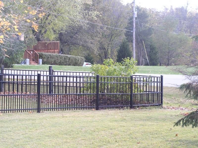 Black metal fence in a yard. Road and house visible in the background.