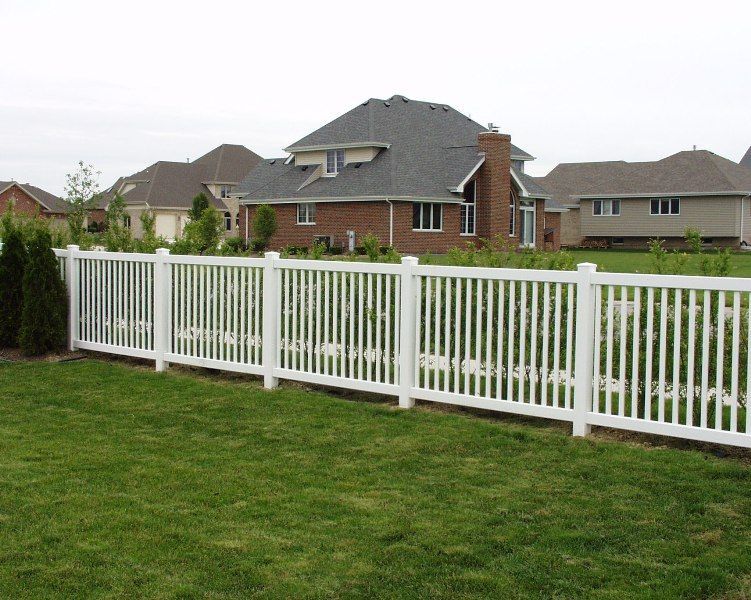 White picket fence in front of a green lawn and houses on a cloudy day.