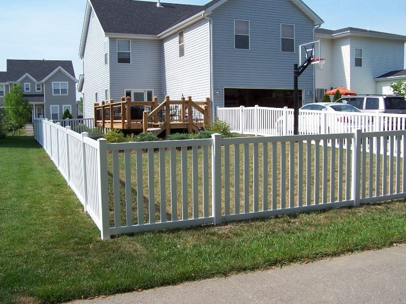 White picket fence surrounds a backyard with a deck and two-story house.